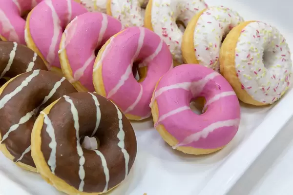 Flatlay shows three different donuts, with chocolate, coloured sprinkles and icing, on a white tray