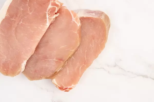 Flatlay von aufgereihten Schweinefleischfilets, auf einer Marmoroberfläche