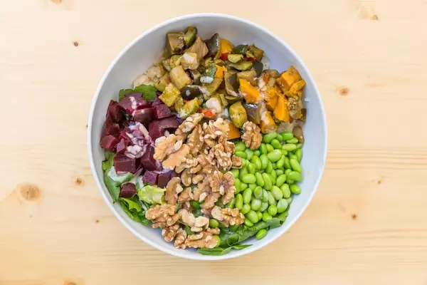 Flatlay von einem veganes Salat mit gegrilltem Gemüse, Edamame, Walnüsse und Soja-Sesam Soße in einer weißer Schale auf einem Holztisch