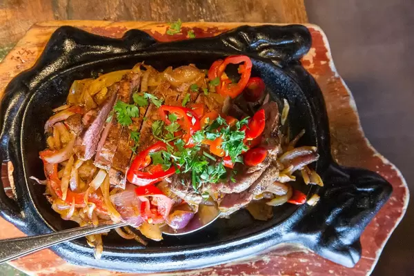 Flatlay von gegrillten Fajitas aus Rinderlende, mit Paprika, grünen Kräutern und Zwiebeln, auf rustikalem Holztisch-Ambiente