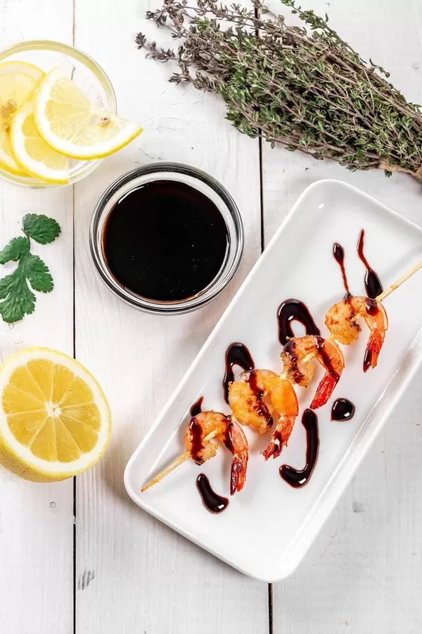 Flatlay von gegrillter Garnele auf weißem Teller mit Sojasoße, Zitrone und Koriander