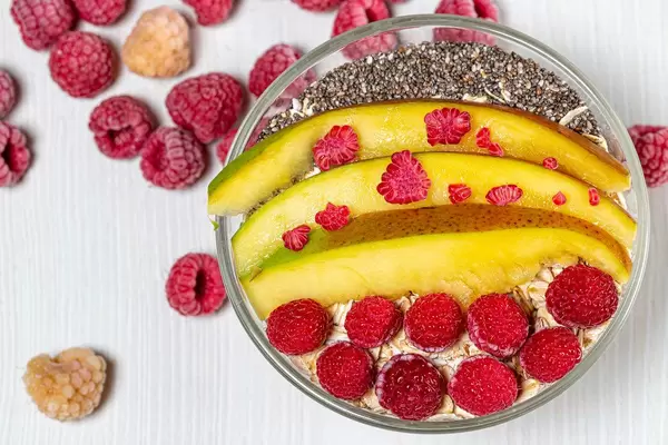 Flatlay von Haferflocken in einer Glasschüssel garniert mit Mango, Himbeeren und Chiasamen