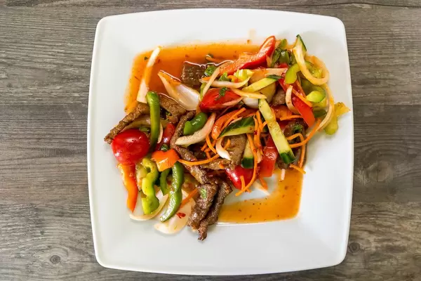 Flatlay zeigt ausgewogenes Thai-Essen mit Rindfleisch, Gemüse, Möhren, Chili, Zitronensaft, Zwiebeln, Koriander und Sellerie und Fischsoße