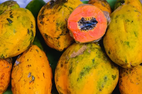 Flatlay zeigt eine aufgeschnittene Papaya-Frucht, die auf anderen Papayas liegt
