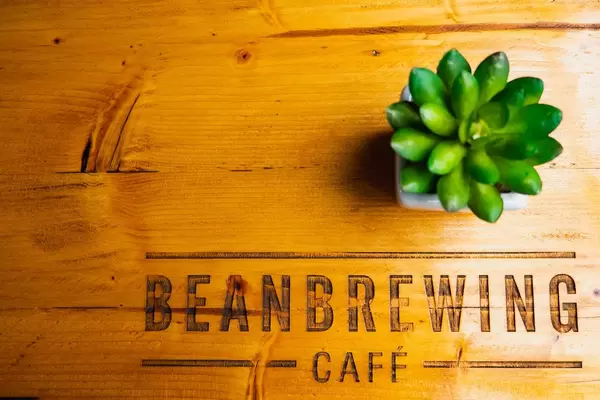 Flatlay zeigt Holztisch mit graviertem Name vom Beanbrewing Café auf den Philippinen und eine kleine Pflanze