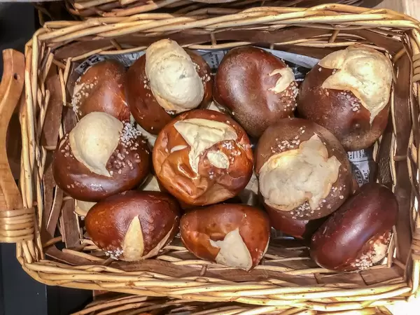 Flatlay zeigt Laugengebäck-Brötchen mit Salz bestreut, in einem Holzkorb
