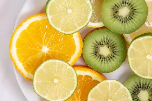 Flatlay zeigt Orangenscheiben, Limonen und Kiwis in Scheiben geschnitten, auf einem Teller