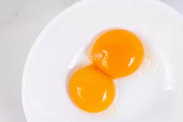 Flatlay zeigt zwei rohe Eigelbe auf einem weißen Teller