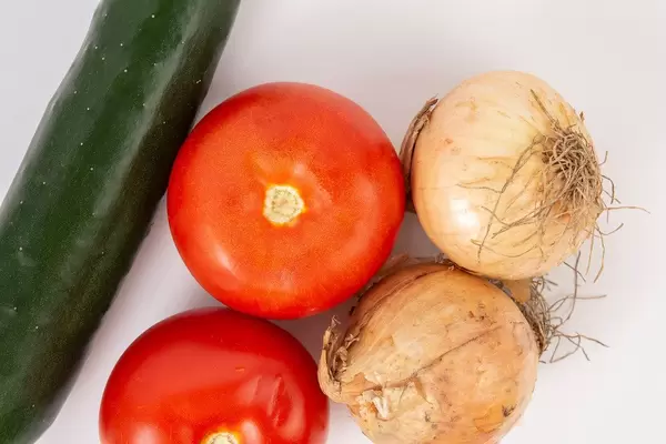 Flatlay zeigt Zwiebelknollen neben Tomaten und einer Salatgurke