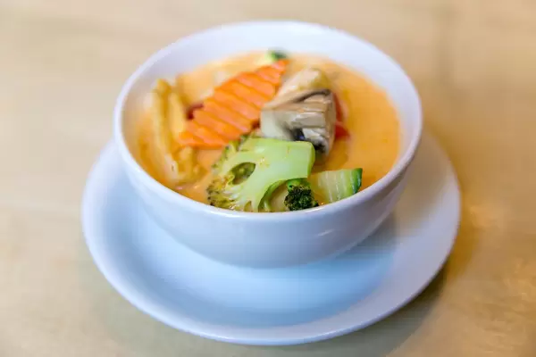 Fleischlose und scharfwürzige Kokosmilchsuppe "Tom Yum" mit  Tofu und frischem Gemüse, in einer weißen Suppenschüssel, als vegane Vorspeise