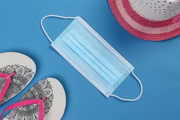 Flipflops with summer beach and medical face mask on blue background