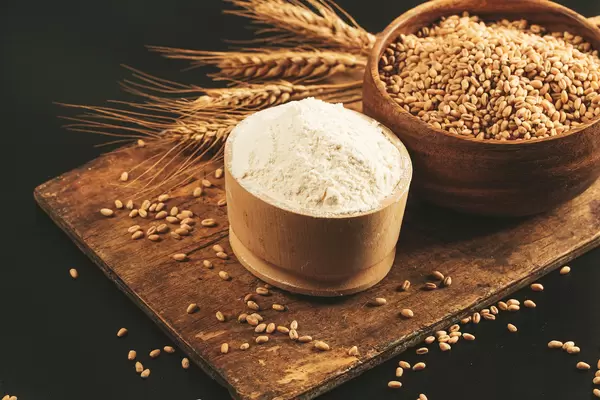 Flour and wheat in wooden bowls on dark background