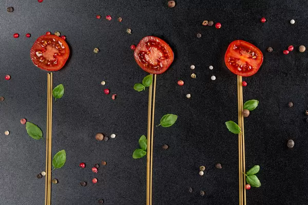 Flowers made from raw spaghetti, tomatoes and basil leaves on black background