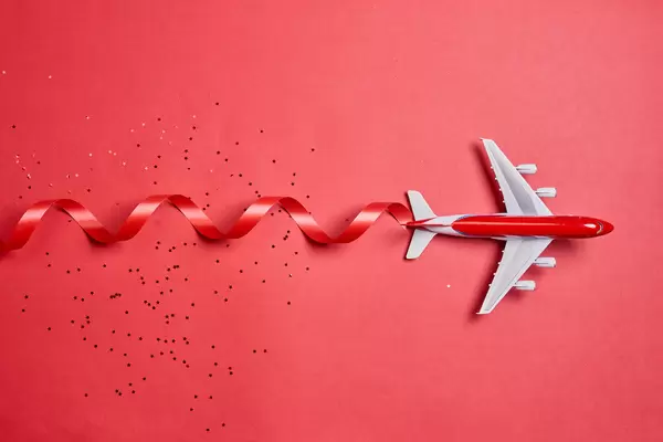 Flying to vacation for Christmas holidays. Airplane on red with festive ribbon
