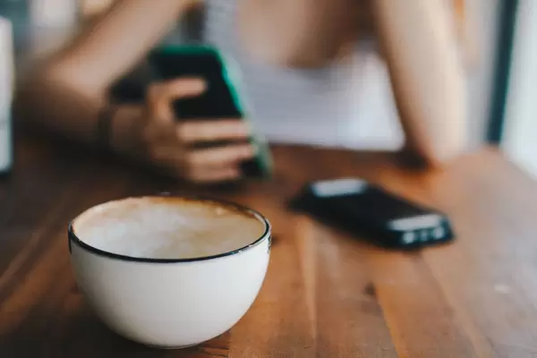 Fokus auf Kaffeetasse. Hand hält ein Smartphone im Hintergrund