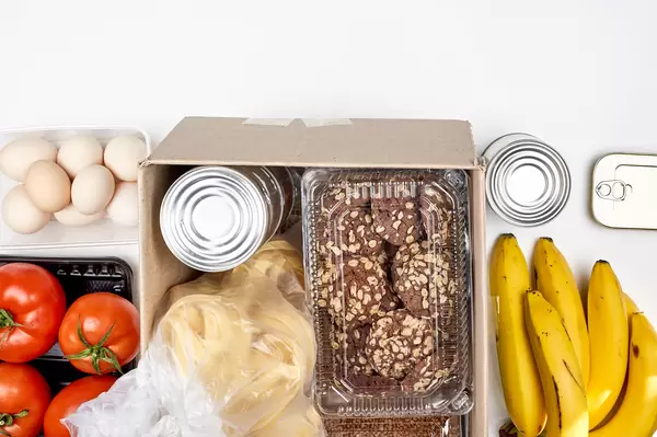 Food bank donation with cookies, tagliatelle noodles, tomatoes, bananas, eggs and tin cans in a box