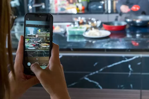 Food blogger: Woman takes cooking show video of the chinese-american chef Martin Yan during a live cooking performance in Germany