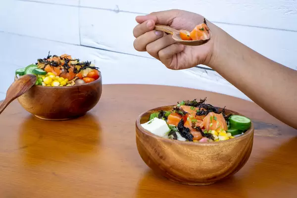 Food Photo of Person eating a Healthy Hawaiian Mixed Poke Bowl Raw Salmon, Tofu and Vegetables with a Wooden Spoon