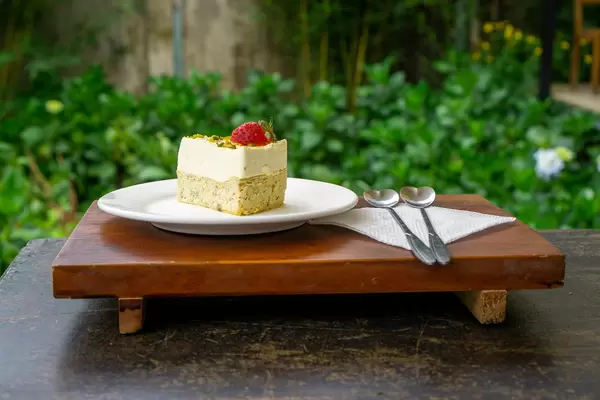 Food Photo of Piece of Cheese Cake with Strawberry and Pistachio on a Wooden Tray with Heart Shaped Spoons and Napkin