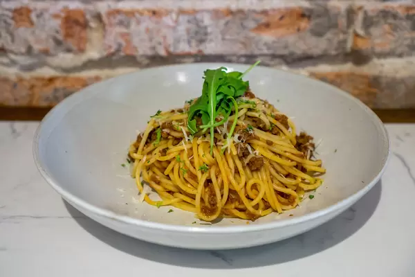 Food Photo of Plate of Spaghetti Bolognese with Grated Cheese and Arugula in a Restaurant