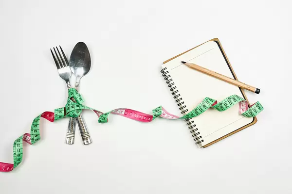 Fork and spoon bowed with measuring tape and empty notepad for diet planning