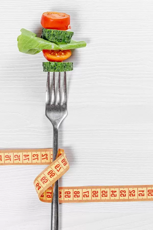 Fork with slices fresh tomato, cucumber, lettuce and measuring tape. The concept care of the figure (Flip 2019)
