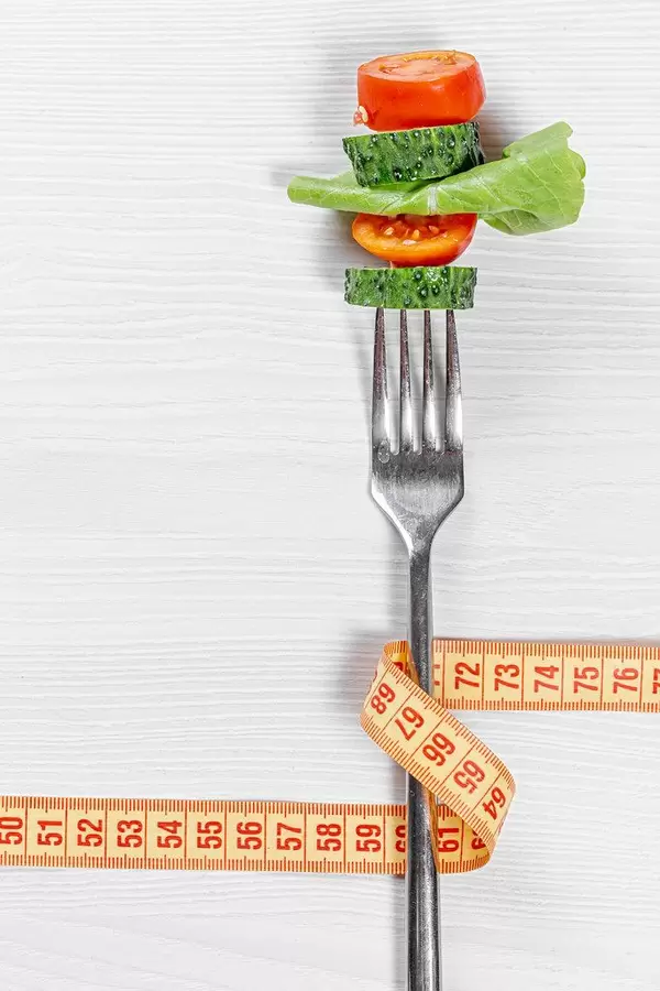 Fork with slices fresh tomato, cucumber, lettuce and measuring tape. The concept care of the figure