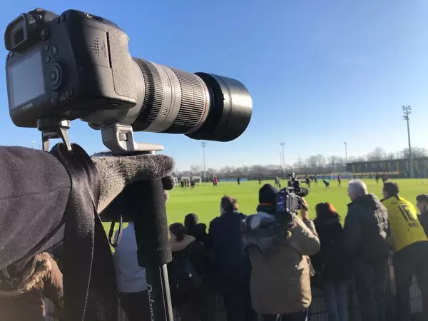 Fotograf mit Canon Kamera und Teleobjektiv am Rande eines Fußballtrainingplatzes