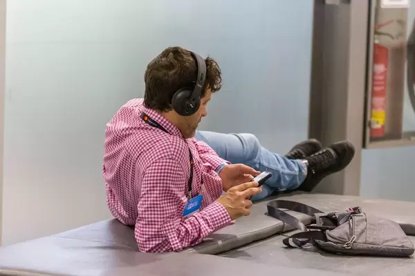 Founders fair visitor taking a break, lies on a couch, looks at his smartphone and wears headphones