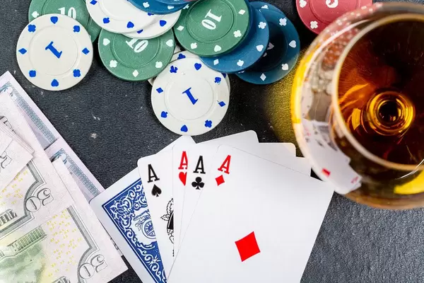Four aces, chips and money on a black table with a glass of cognac. Top view