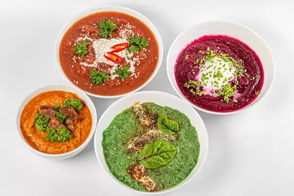 Four bowls with delicious vegetable soups on a white background