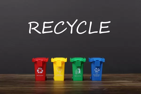 Four colorful recycle bins on wooden table with Recycle text