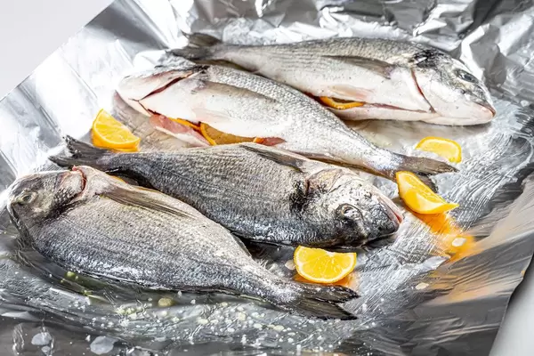 Four raw fish with spices and lemon slices on foil (Flip 2020)