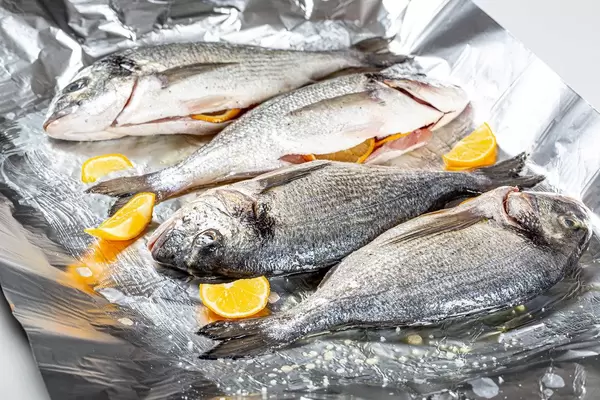 Four raw fish with spices and lemon slices on foil