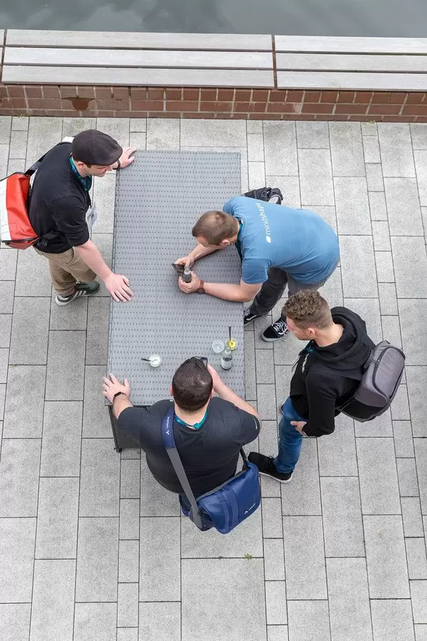Four young men standing around a rattan table with smartphones and drinks on a terrace of the AXA-building at the Barcamp OMWest19 in Cologne.