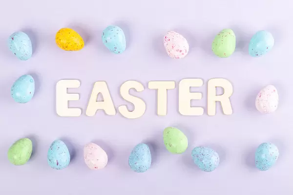 Frame of multicolored chocolate eggs on a purple background with the inscription easter from wooden letters