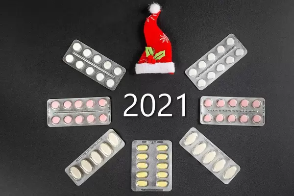 Frame of pills in blisters and santa hat on a black background with the inscription 2021 in the center