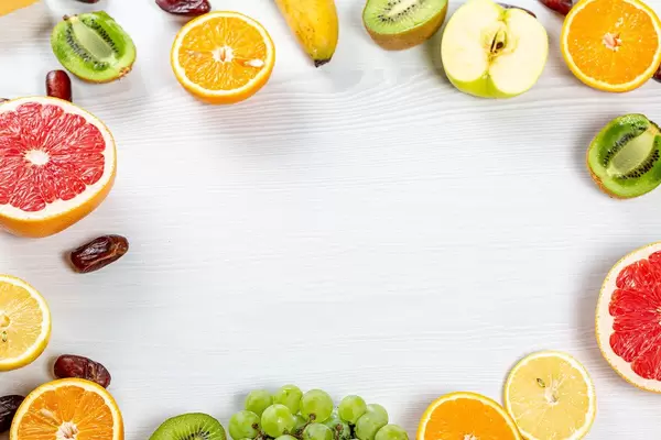 Frame with colorful fresh fruit and dried dates on white wooden background with free space in the middle