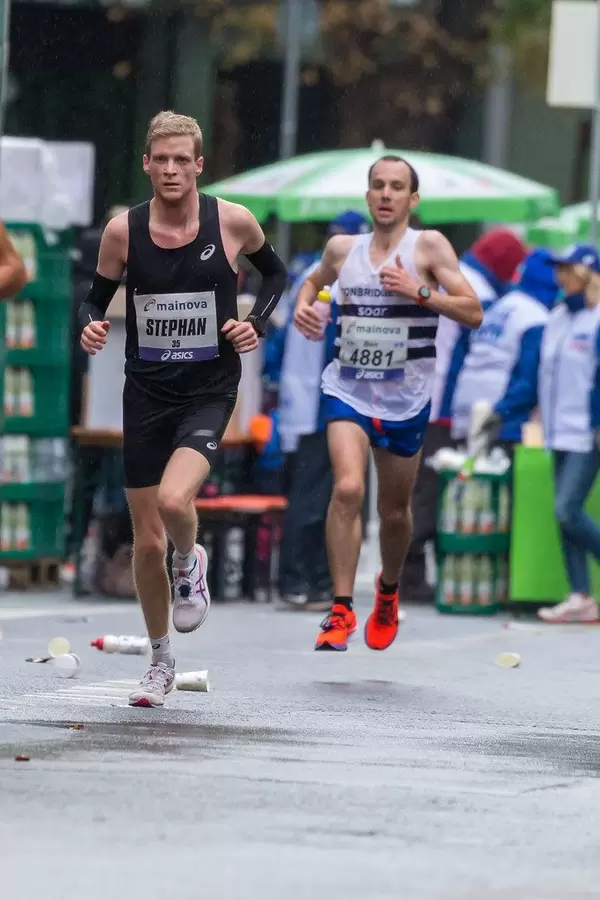 Frankfurter Marathon: Zwei fitte Athleten laufen hintereinander hinter einer Verpflegungsstation