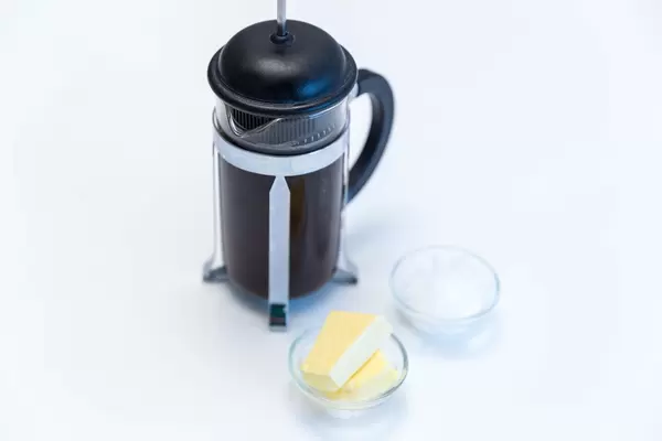 Französischer Kaffeebereiter neben einer Glasschale mit Butter und Eiswürfel