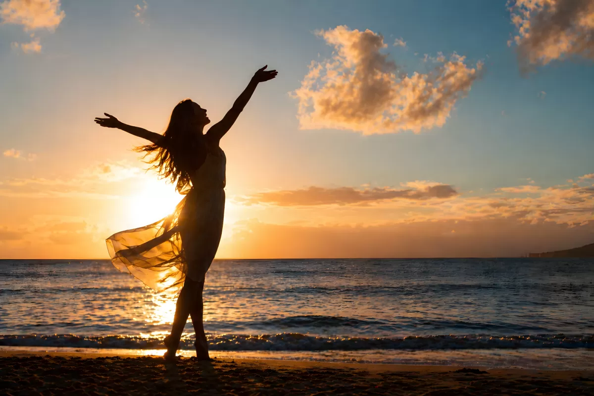 Frau am Strand tanzt bei strahlendem Sonnenuntergang