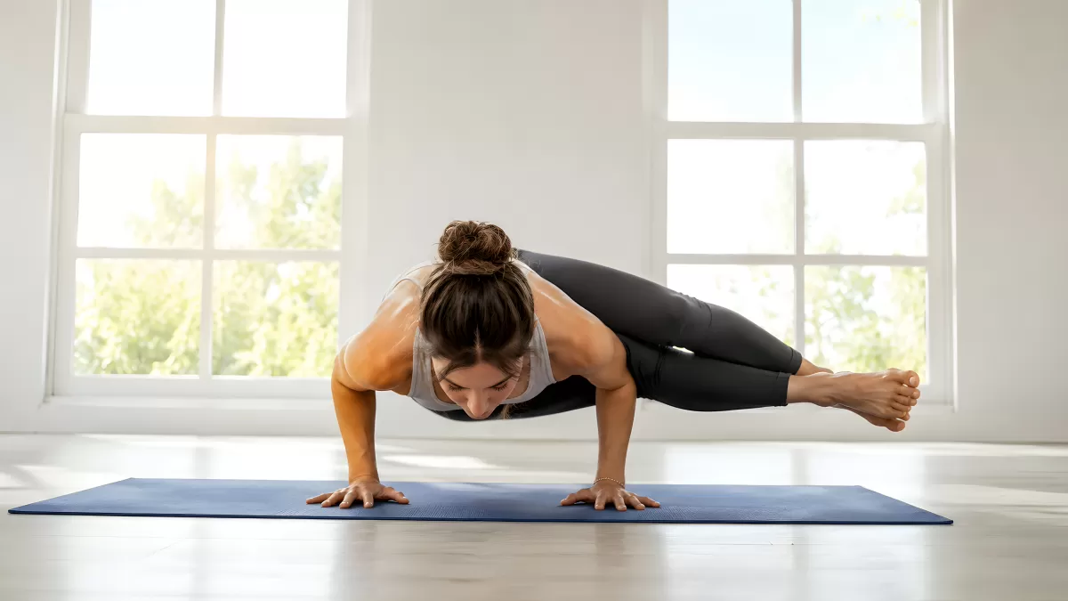 Frau balanciert in Arm-Balance-Yogapose auf blauer Matte
