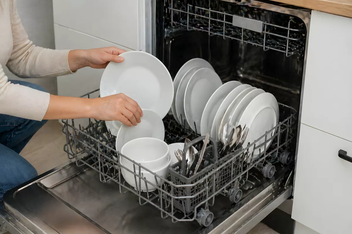 Frau befüllt Spülmaschine mit weißem Geschirr