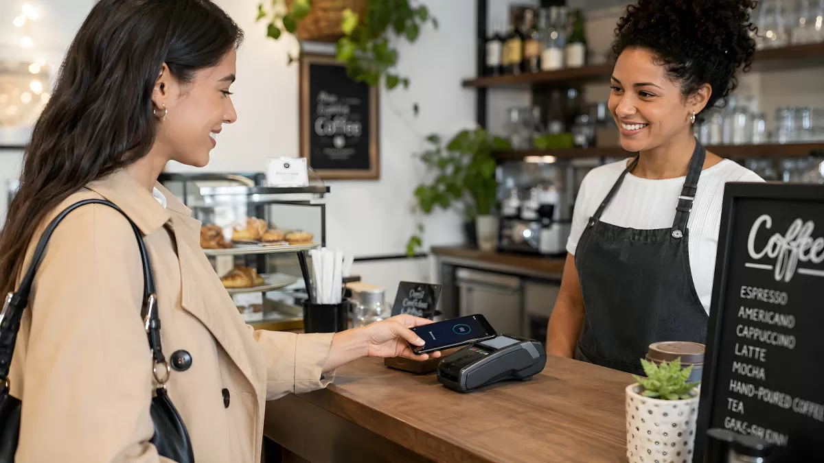 Frau bezahlt kontaktlos per Smartphone im Café