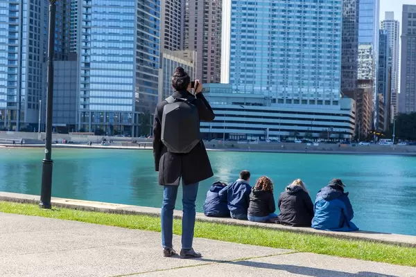 Frau fotografiert die Wolkenkratzer in Downtown Chicago mit ihrem Smartphone, während andere Menschen am Wasser sitzen