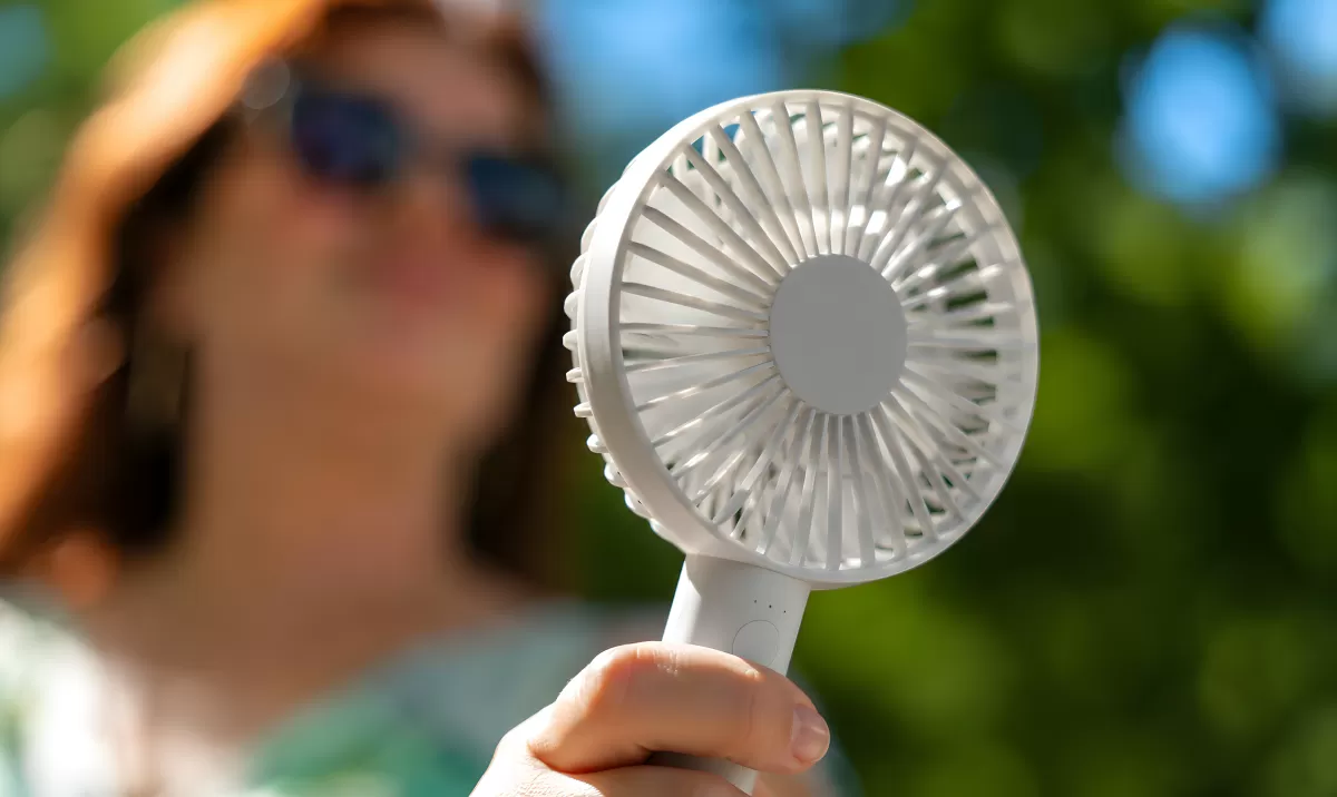 Frau hält Mini-Ventilator im Freien an heißem Sommertag