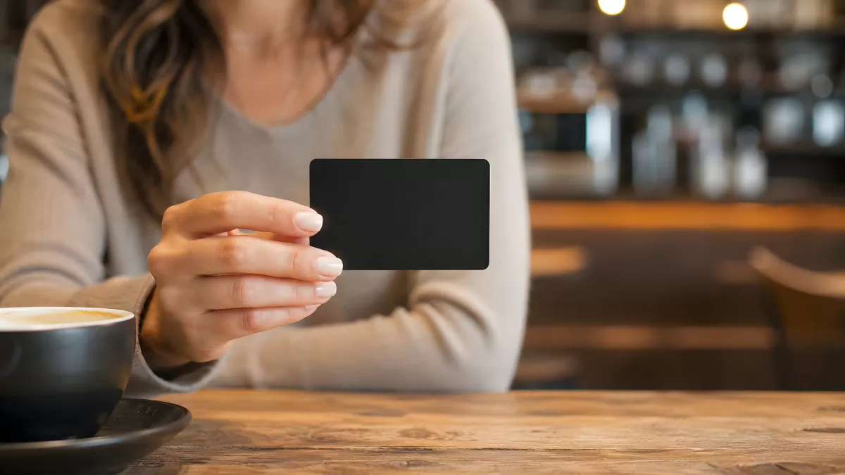 Frau hält schwarze Kreditkarte im Café mit Kaffeetasse