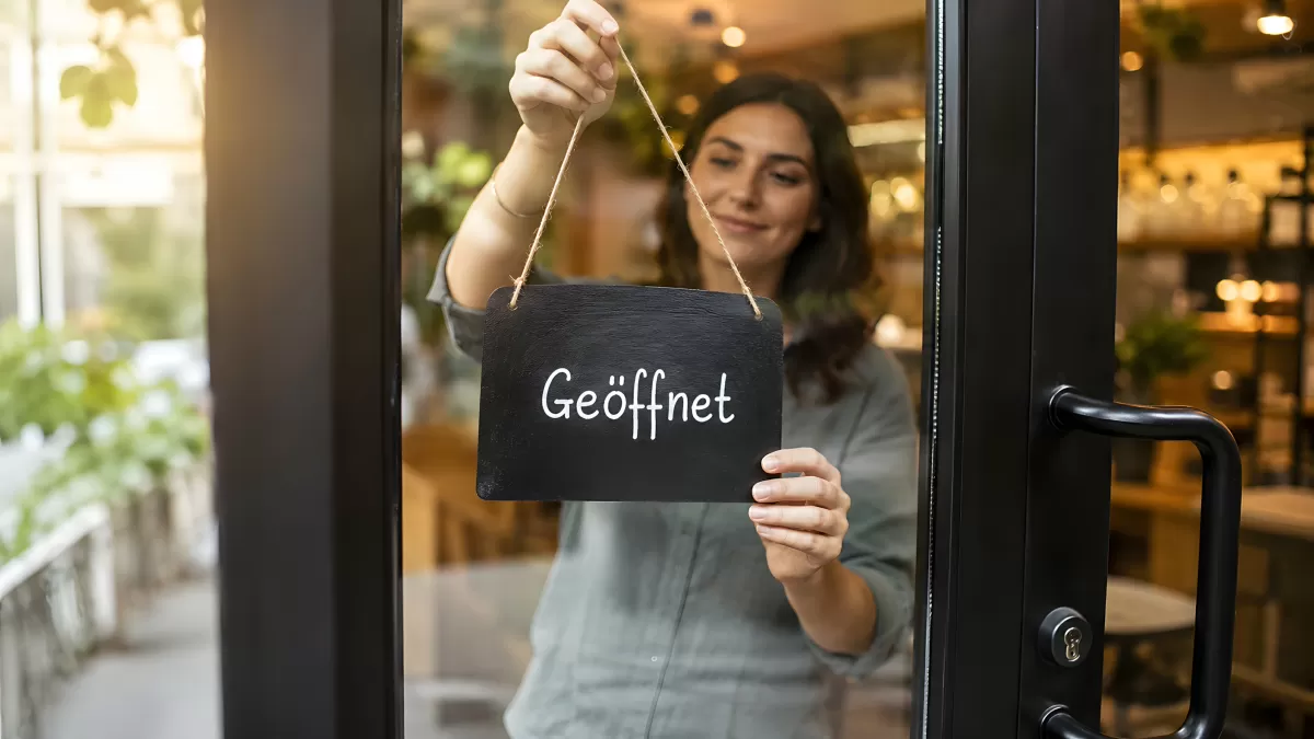 Frau hängt Geöffnet-Schild an Café-Eingangstür