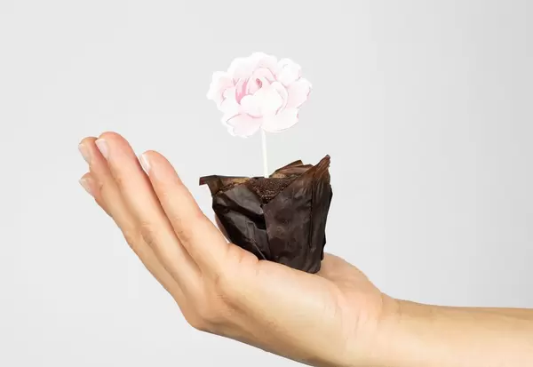 Frau hält einen Muffin mit Blumendekor in der Hand