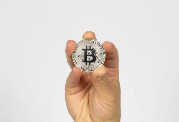 Frau hält einen silbernen Bitcoin in der Hand